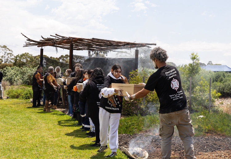 A queue of young Aboriginal men and women pass along boxes to be smoked before reburial